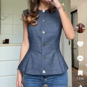 Mörkblå jeansväst från Zara - Snygg mörkblå jeansväst från Zara med silvriga knappar framtill. Västen har en figurnära passform, är ärmlös och har en lätt utsvängd nederdel. Perfekt att styla med dina favoritjeans för en cool look.