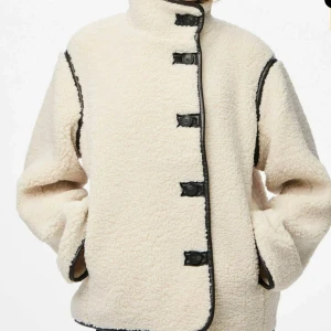 Beige teddyjacka med svarta detaljer - Säljer en beige teddyjacka med svarta kantdetaljer och stora knappar framtill. Använd fåtal gånger ✨