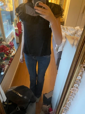 Svart blus med volang och prickig mesh💞 - Säljer en svart blus med transparent mesh upptill och små prickar. Blusen har volangdetaljer runt halsen och axlarna, samt korta ärmar. Materialet känns lätt och luftigt, perfekt för dig som gillar söta detaljer och en cool vibe. Jätte bra fest topp ❣️