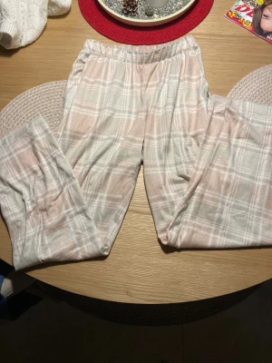 Rutig mjukisbyxa XS från Passion - Supermysiga mjukisbyxor från Passion i storlek XS med ett ljust rutigt mönster i beige och vitt. Byxorna har elastisk midja och är tillverkade i mjukt material som känns skönt mot huden. Perfekta för chill hemma eller när du vill vara extra bekväm.