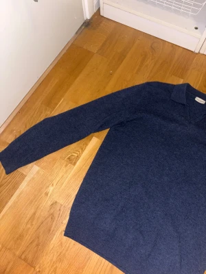 Blå stickad polotröja John Henric - Mörkblå cashmere polotröja från John Henric i storlek M. Tröjan har klassisk krage med v-ringning och långa ärmar. Mjuk och skön kvalitet som passar perfekt när det är lite kyligare ute. Enkel och stilren design utan mönster.