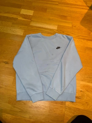 Nike sweatshirt  - Ljusblå sweatshirt från Nike i storlek S. Tröjan har klassisk rund hals, långärmade ärmar och en liten svart Nike-logga på bröstet. Tillverkad i mjuk bomull med ribbade muddar vid ärmslut och nederkant. Perfekt för chill dagar eller när du vill ha en clean look. Enstaka fläckar som går att få bort med vanish. 