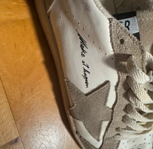 Golden Goose Ball Star sneakers beige - Golden Goose Ball Star sneakers i beige och vitt med GGDB-logga på plösen och textdetaljer som 'Make it happen' på sidan. Skorna har en stor stjärna i mocka, snörning och platt sula. Kombination av skinn och mocka ger en cool och sportig vibe.