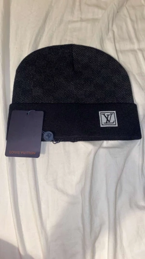 Svart mössa - Snygg svart och grå mössa med klassiskt rutigt mönster. Mössan är stickad och har en vikt kant. Perfekt accessoar för att lyfta din vinterstil.