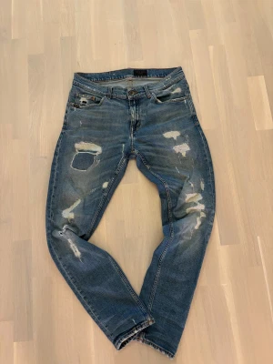 Slitna tiger of Sweden jeans - Säljer ett par blå jeans från TJ med snygga slitningar och patchade hål både fram och bak. Jeansen har klassisk femficksdesign, normal passform och är tillverkade i jeansmaterial. Perfekt för dig som gillar en rå och avslappnad stil.
