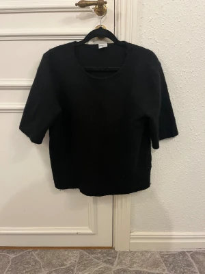 Svart stickad tröja från Stories M - Svart stickad tröja från Stories i storlek M (40-42). Tröjan har rund hals, korta ärmar och en loose passform. Mjuk och fluffig känsla, perfekt för dig som gillar enkel och stilren look. Passar till både jeans och mjukisbyxor.