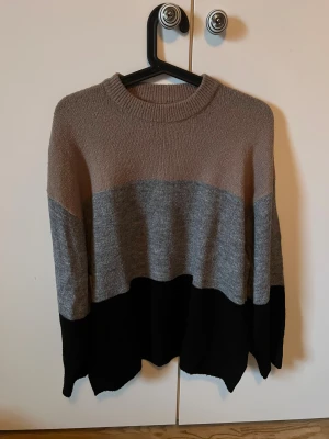 Randig stickad tröja från Lager 157 - Säljer en stickad tröja från Lager 157 i storlek S. Tröjan har breda blockränder i beige, grått och svart, rund halsringning och lång ärm. Perfekt för dig som gillar en chill och avslappnad stil.