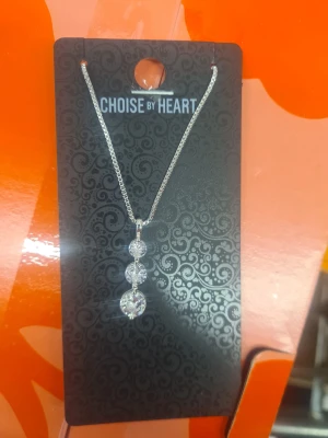 Silverfärgat halsband med glittriga stenar - Snyggt halsband från Choise by Heart med tunn silverfärgad kedja och hängsmycke med tre runda, glittriga stenar i rad. Perfekt för dig som gillar stilrena och glittriga detaljer. Kedjan är enkel och smycket ger en elegant touch till din outfit.