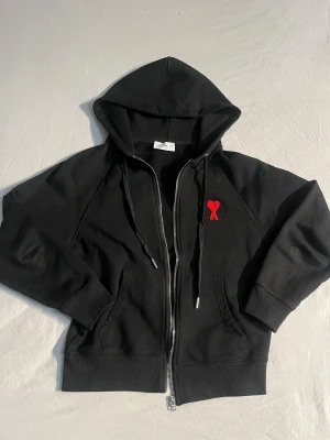 Svart hoodie från Ami Paris med rött hjärta - Svart hoodie från Ami Paris med dragkedja. Bara använt fåtal gånger. Säljer pga att den är för liten för mig.