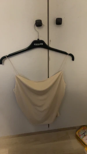 Beige linnetopp med draperad front - Säljer en stilren beige linnetopp från Gina trio t med tunna axelband och snyggt draperad front. Toppen har en mjuk, flowy passform och är perfekt för dig som gillar minimalistisk stil. Materialet känns lätt och skönt mot huden.