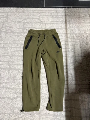 Nike Tech Byxor - Nike tech byxor i färgen grön Storlek S. Byxorna är i nya modellen med öppna ben som har svart spännen. Dom är helt felfria. 