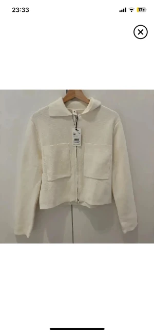 Vit stickad overshirt från Åhlens - Snygg vit stickad overshirt från Åhlens med krage, två stora fickor framtill och dragkedja. Jackan har en clean och modern look med rak passform och långa ärmar. Perfekt för dig som gillar minimalistisk stil och vill ha något som sticker ut. Helt ny