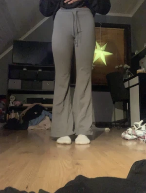 Grå bootcut mjukisbyxor med snörning - Säljer ett par grå mjukisbyxor med bootcut och snörning i midjan. Byxorna har hög midja och är tillverkade i mjukt material som sitter skönt mot kroppen. Perfekt för chill dagar och har en loose passform nedtill.