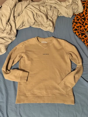 Beige sweatshirt  - Säljer en stilren beige sweatshirt från Les Deux med svart broderad logga på bröstet. Tröjan har rund hals, ribbade muddar och är långärmad. Perfekt för dig som gillar enkel och clean design. Materialet är mjuk bomull som känns skönt mot huden. Går alltid att diskutera om pris 