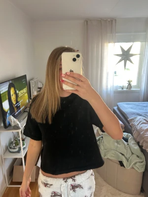 Svart croppad t-shirt topp - En enkel svart croppad t-shirt topp med korta ärmar och rund hals. Modellen är loose fit och har en mjuk, lite fluffig yta som ger en mysig känsla. Perfekt för chill dagar och att matcha med jeans eller mjukisbyxor.