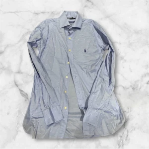 Blå prickig skjorta från Ralph Lauren - Snygg ljusblå skjorta från Ralph Lauren med små vita prickar och klassisk krage. Perfekt för dig som gillar stilrena detaljer och ett fräscht uttryck. Riktigt bra skick Passar M.