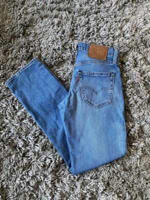Levi's 511 blå jeans W28 L30 - Säljer ett par klassiska Levi's 511 jeans i ljusblå denim. Modellen har raka ben, fem fickor och den ikoniska läderpatchen bak i midjan. Perfekt passform och snygg tvätt som funkar till allt. Materialet är 100% bomull.