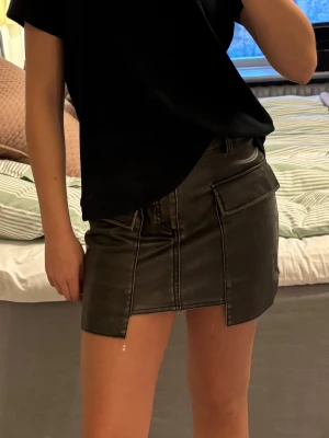 Skinnkjol med fickor - Kort skinnkjol med markerade sömmar och stora fickor framtill. 