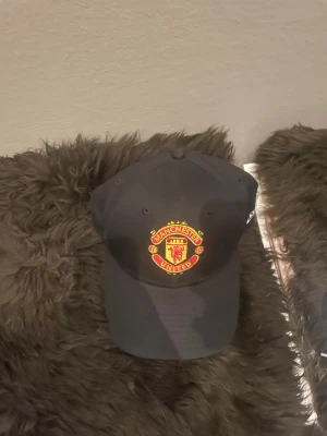 Manchester United svart keps 9FORTY - Svart keps från New Era, modell 9FORTY, med Manchester Uniteds broderade klubbmärke i rött och gult framtill. Justerbar metallspänne baktill och böjd skärm. Perfekt för dig som vill visa ditt stöd för United på matchen eller i stan. Den är aldrig använd.