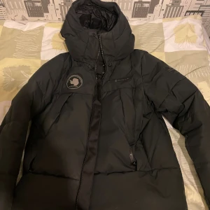  Sail Racing svart vinterjacka - Säljer en svart dunjacka från Sail Racing i storlek S, köpt för 5700kr. Jackan har hög krage, stor huva och dragkedja framtill. Märkets logga och patch på bröstet och ärmen ger en clean look. Perfekt för kalla dagar med sin tjocka vaddering och sportiga design. Hör av er för intresse och bilder när den väl sitter på!