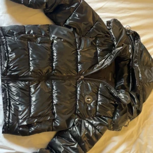 Svart pufferjacka från Trapstar S - Svart glansig jacka från trapstar i storlek S, passar även M. Luvan går att ta av, midjan går o justera. Den har ett litet hål vid fickan men syns inte om man inte letar, annars i väldigt bra skick. Kontakta mig vid minsta lilla fundering!