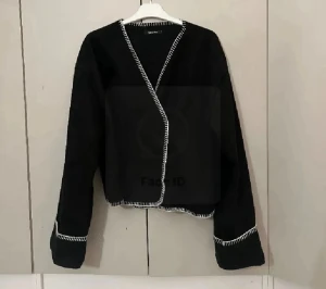 Svart omlottkofta med vita detaljer - Ena knappen är av och den andra finns men fungerar ej men jackan går att använda som en kofta osv oxå 