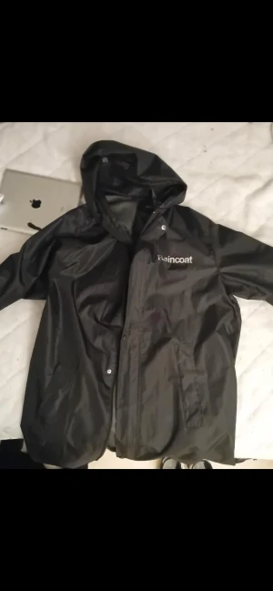 Svart regnjacka från Vetements x Tricots Pour Femme 2017 Collaboration - Svart regnjacka från Vetements x Tricots, med huva och tryckta texter både fram och bak. Jackan har långa ärmar, snörning vid huvan och knappar längs fronten. Materialet är syntetiskt och vattenavvisande, perfekt för blöta dagar. Aldrig använda mer än att testat inomhus, aldrig haft den ute. Nypris ligger på 4-5000 kr. Ganska ovanlig bara ett fåtal gjorda. Storlek L/XL