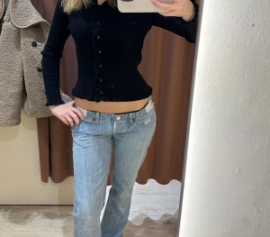 Vivienne Westwood jeans - Säljer ett par ljusblå jeans från Vivienne Westwood med låg midja och bootcut fit. Jeansen har slitna detaljer och fransade kanter både fram och bak, vilket ger en cool och edgy vibe. Klassisk femficksmodell med knapp och dragkedja.