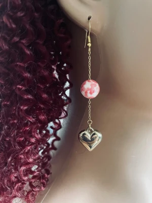 By prisförslag- 1 st Guldörhänge med hjärta och pärla - Unikt örhänge med tunn guldfärgad kedja, en rund pärla i rosa och vitt samt ett hängande hjärta i guldton. Perfekt statement-piece för dig som gillar lekfulla detaljer och romantiska vibbar.