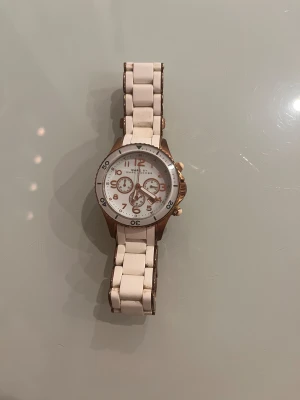 Vit och guld klocka Marc by Marc Jacobs - Snygg klocka från Marc by Marc Jacobs med vit länkarmband och detaljer i guld. Rund urtavla med tre små kronografer och tydliga siffror i guld. Klockan har en stilren och modern design som sticker ut med sin kombination av vitt och guld. Behov av batteribyte. Kvitto finns 