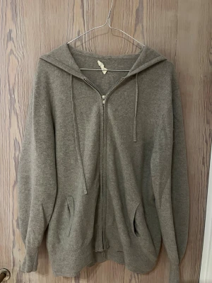Beige hoodie i kashmir från Soft Goat - Mysig beige hoodie från Soft Goat i mjuk kashmir. Tröjan har dragkedja, huva med snörning och fickor fram. Mockadetaljer på armbågarna är tillagda och den har ett litet hål på höger armbåge, pris kan diskuteras!
