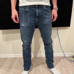 Tiger of Sweden jeans - Snygga tiger of Sweden jeans i klassisk blå färg med lätt slitning. Modellen är slim fit med raka ben och normal midja. Jeansen har fem fickor, bruna detaljer och tiger of  Sweden patch bak. Perfekt passform och stilren look.