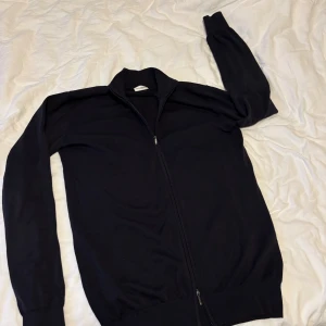 John Henric med dragkedja - Snygg svart kofta från John Henric i storlek S. Tröjan har hel dragkedja framtill, ribbad krage och muddar vid ärmslut och nederkant. Materialet är stickat och känns mjukt mot huden. Perfekt för lager-på-lager och chill stil.