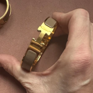 Helt ny!  armband ljusbrun färg - Säljer ett nytt Clic H-armband i guld med ljusbrun färg. Armbandet har en stilren, rundad form och den klassiska H-detaljen framtill. Perfekt för dig som gillar lyxiga accessoarer med minimalistisk vibe.