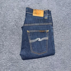Nudie Jeans - Mörkblå Nudie Jeans Thin Finn med skinny passform och klassisk femficksdesign. Tillverkade i stretchigt jeanstyg för skön känsla och stilren look. Midja 33cm, längd 101cm.  Ifall det inte finns någon bild i annonsen där jag bär plaggen jag säljer så är det för att jag ej kan ha storleken heller passformen, så kolla måtten för storlek och googla på modellnamnet för passform 😉41