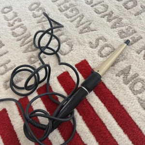 Nano Titanium Curling Wand - Professionell locktång med nano titanium-teknologi för jämn värme och skonsam styling. Konformad design för naturliga lockar. Svart handtag, guld värmedel, och lång sladd. Fint skick, inga synliga defekter eller slitage.