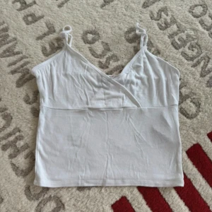 Vit omlott-linnetopp från Gina Tricot - Säljer en vit omlott-linnetopp från Gina Tricot med smala axelband och v-ringning. Toppen är i mjuk bomull och har en enkel, clean look som är perfekt till sommaren. Snygg att styla med jeans eller kjol för en fräsch vibe.