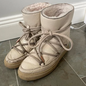 Beiga Inuikii skor i skinn - Exklusiva skor från Inuikii i färgen cream. Tillverkade i äkta läder med pälsfodrad insida. Klassisk snörning framtill och broderad logga baktill. Säljes i använt och befintligt skick, såsom bilderna. ✔ Äkta läder ✔ Inuikii sula – helt oanvänd ✔ Nypris: 3 699 kr