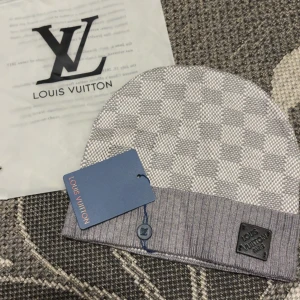Grå rutig mössa från Louis Vuitton - Snygg grå mössa från Louis Vuitton med klassiskt rutigt mönster och ribbad kant. Märkeslogga i metall på kanten och diskret LV-knapp. Perfekt accessoar för dig som vill ha en lyxig och stilren look under kalla dagar.