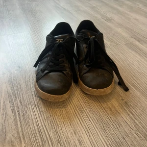 Svarta sneakers från Polo Ralph Lauren - Svarta sneakers från Polo Ralph Lauren med klassisk logga på sidan och Polo-tryck bak. Skorna har snörning, rund tå och vit sula. Ovandelen är i 100% skinn och insidan i textil. Perfekta för en stilren och sportig look.