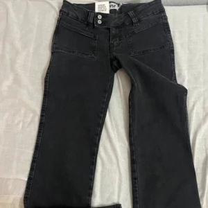 Gråa lager 157 low waist bootcut jeans - Snygga jeans med bootcut passform och klassiska fem fickor. Jeansen har dubbla knappar i midjan och är tillverkade i slitstarkt jeansmaterial. Perfekta för dig som gillar en tidlös look med lite extra edge. Köpt för 400
