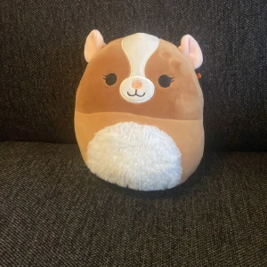 Gosedjur  - Bilderna visar ett mjukisdjur i form av en hamster, troligen en Squishmallow. Produkten är mjuk, rund och har ett sött ansikte. Inga synliga elektronikfunktioner eller märken relaterade till elektronik. Produkten verkar vara i gott skick utan synliga defekter.