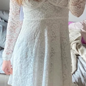 Vit spetsklänning med lång ärm - Superfin vit kort spetsklänning från bubbleroom med v-ringning och långa ärmar. Klänningen har blommigt spetsmönster och markerad midja som ger en snygg siluett. Perfekt för dig som vill ha en romantisk och trendig look.