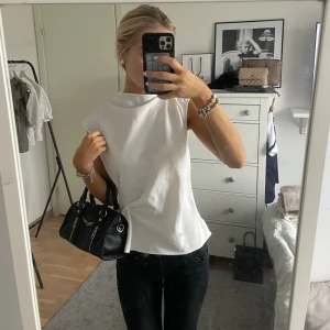 Vit blus med knappar från Zara - Säljer en vit blus från Zara med coola axelvinklar och knappar längs hela ryggen. Blusen är ärmlös och har en öppen ryggdetalj som ger en unik look. Perfekt till svarta jeans eller kjol för en clean och trendig stil.