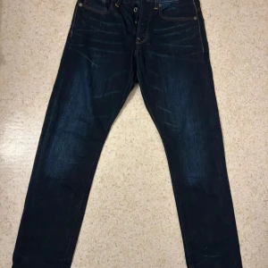 Mörkblå jeans från G-Star RAW, 30/32 - Snygga mörkblå jeans från G-Star RAW i klassisk femficksmodell med kontrastsömmar och raka ben. Jeansen har en normal passform och är tillverkade i slitstarkt denim. Perfekt för dig som gillar stilrena och tidlösa jeans. Endast testade! 