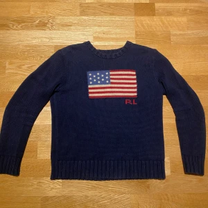 Mörkblå stickad tröja Polo Ralph Lauren - Snygg mörkblå stickad tröja från Polo Ralph Lauren med amerikansk flagga i rött, vitt och blått på bröstet samt RL-broderi. Rund hals och ribbade muddar vid ärmslut och nederkant. Inga hål och den är i jätte bra skick. 