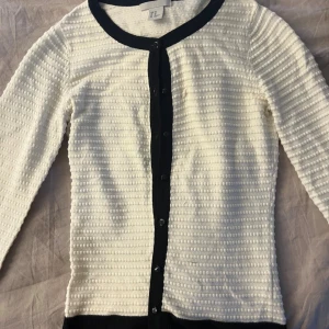 Vit kofta med svarta detaljer och trekvartsarmar från hm - Säljer en vit kofta från H&M i storlek XS med svarta kanter och knappar framtill och trekvartsarmar. I nästan helt nytt skick använd två gånger 