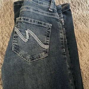 Mörkblå jeans från Nelly med broderad ficka - Snygga mörkblå jeans från Nelly med vit broderad detalj på bakfickan. Klassisk femficksmodell, hög midja och raka ben. Jeansen har tydliga kontrastsömmar och är tillverkade i mjukt denimtyg som sitter skönt hela dagen.