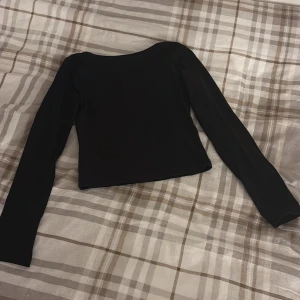 Svart croppad långärmad topp - En stilren svart croppad topp med lång ärm och rundad urringning. Perfekt att matcha med höga jeans eller kjol för en clean look. Enkel design utan mönster eller detaljer, vilket gör den lätt att styla.