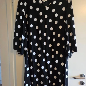 Svart prickig klänning Cellbes, stl 46/48 - helt ny - Svart klänning från Cellbes med stora vita prickar och v-ringad hals. Klänningen har trekvartsärm och är tillverkad i mjuk och skön viskos. Perfekt för dig som gillar ett lekfullt mönster och vill ha en bekväm och snygg look.
